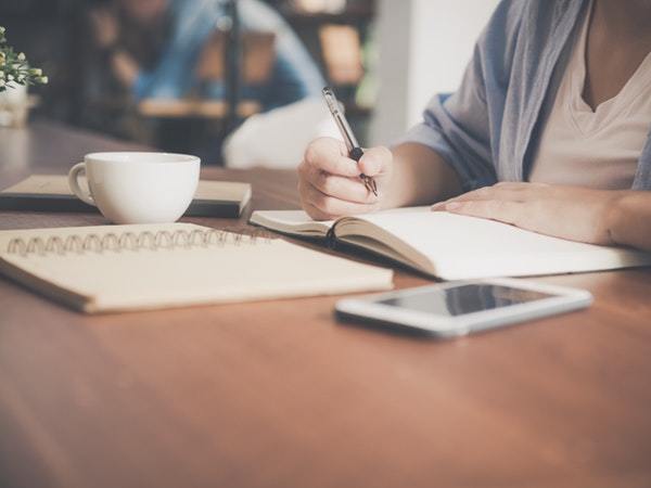 woman-writing-on-a-notebook-beside-teacup-and-tablet-733856 (1)